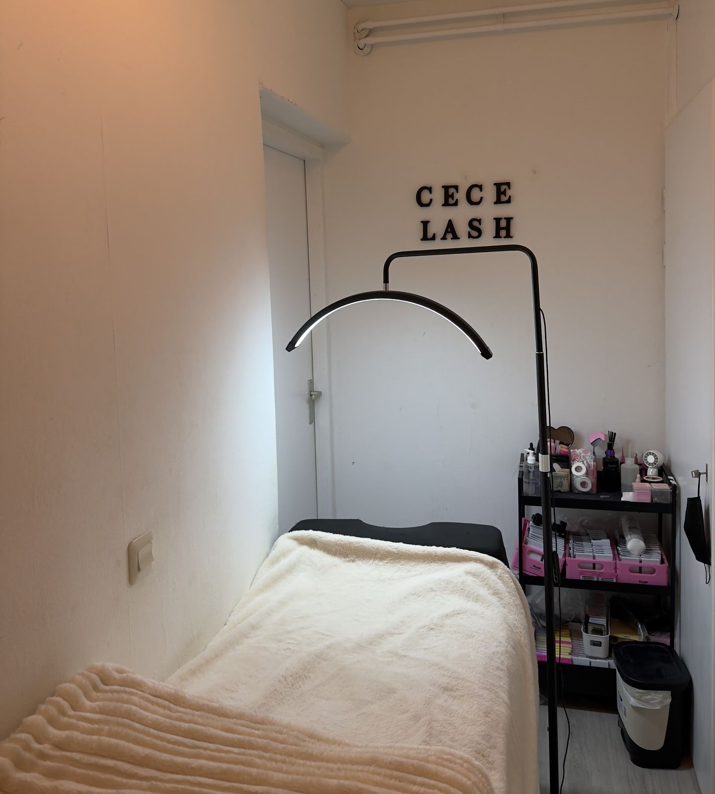 De studio van Cece Lashh: een ligbed met een zachte deken, de lash lamp en de letters CECE LASH aan de muur